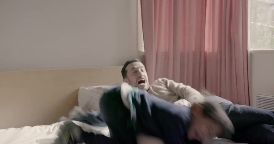Boy holds pillow over man's face as they play