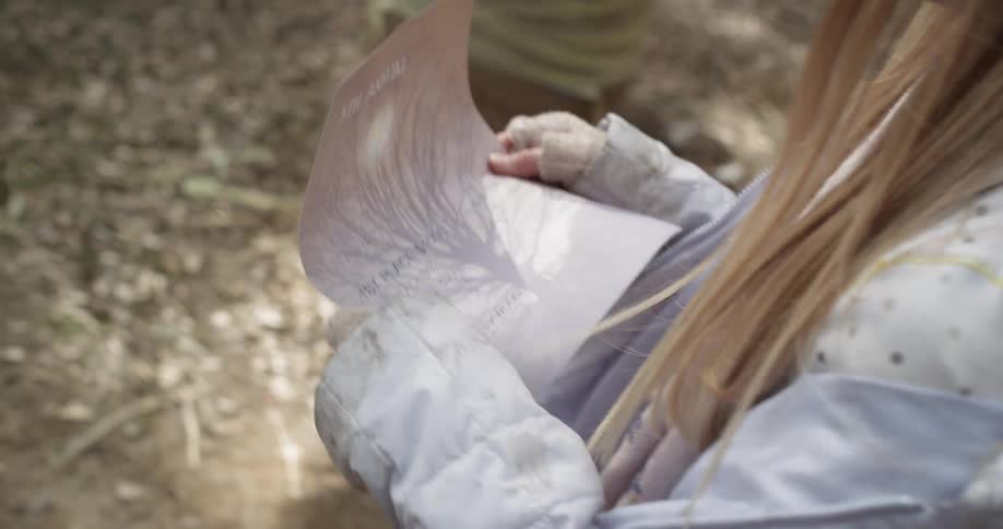 A young girl carries a piece of paper in the woods