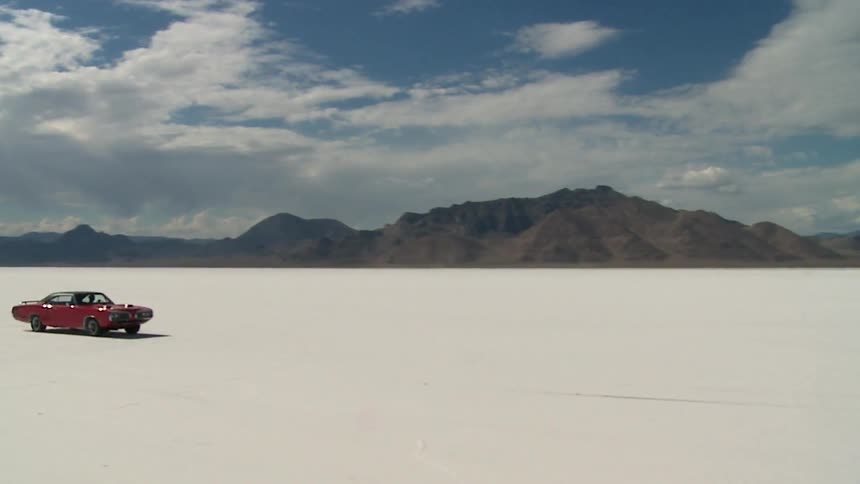 A red sports car drives across salt flats