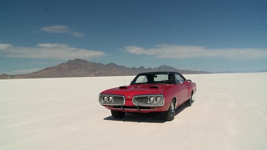 A late model american car is driving on a salt flat in the desert