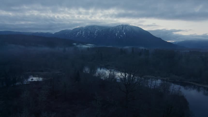 A frozen landscape has a river and a mountain in the background