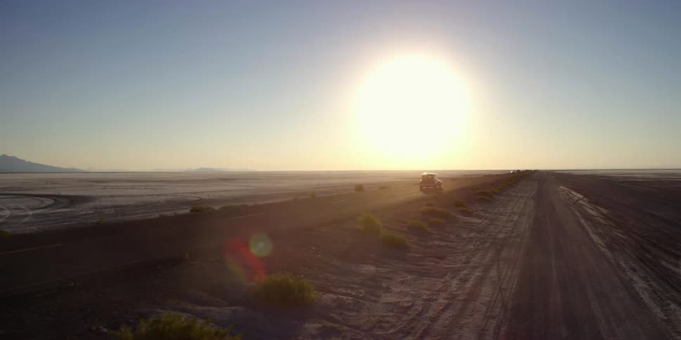The sun is ready to set over this long field as a truck races down the road