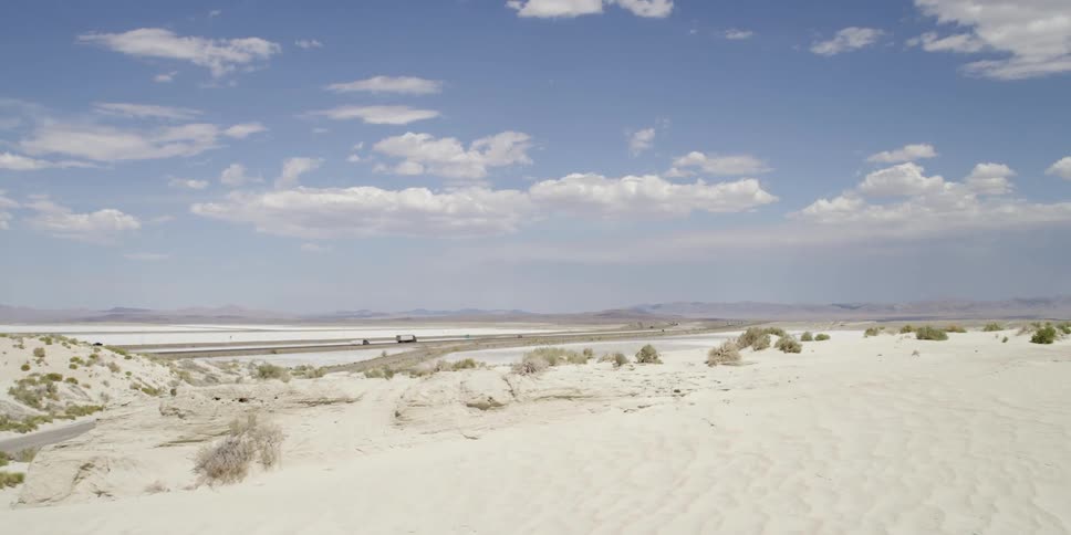 Vehicles are driving on a highway in a desert filled with sand dunes on a sunny day