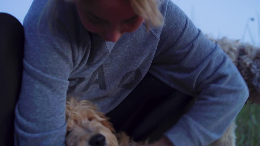 A woman is hugging one of her dogs outside at dusk