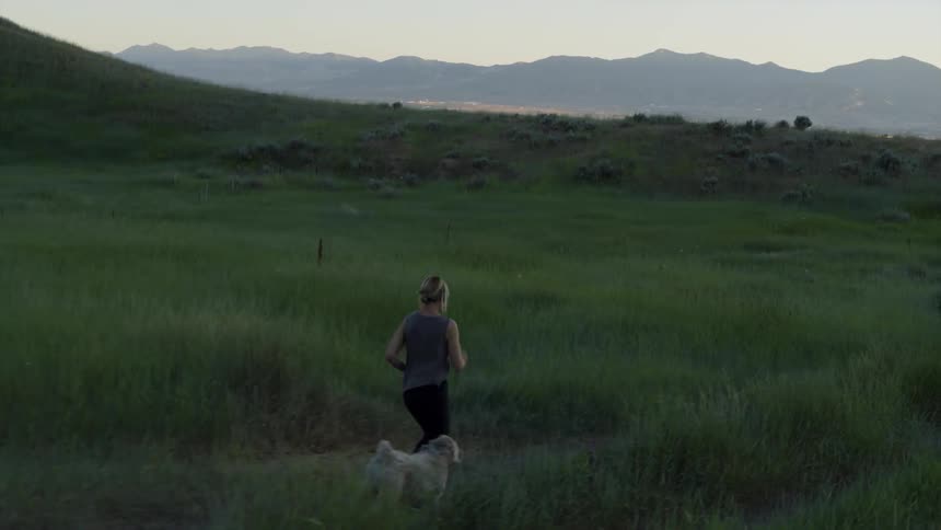 A woman is running down a dirt path with her two dogs