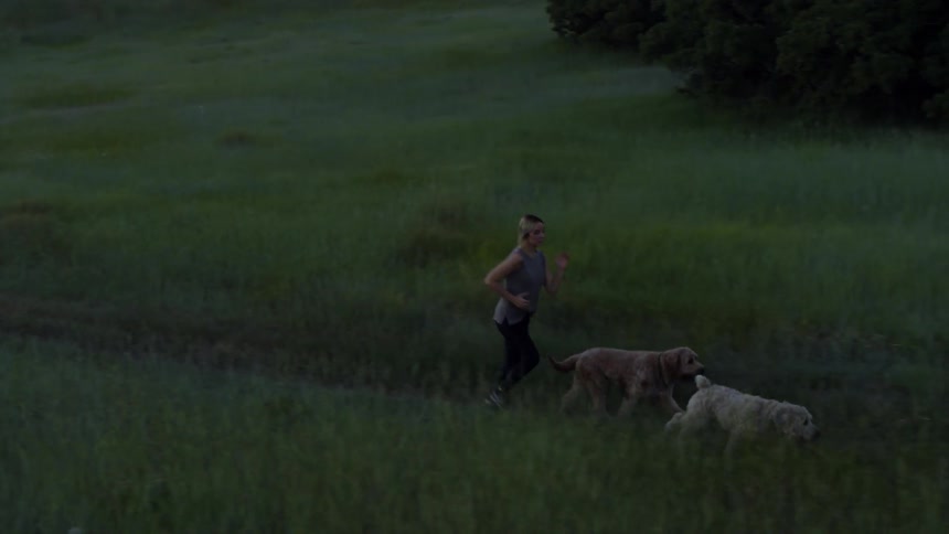 A woman runs right behind her two dogs
