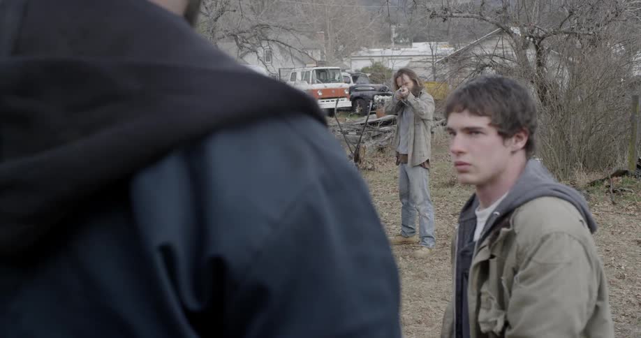 A man is pointing a gun at another man in the woods