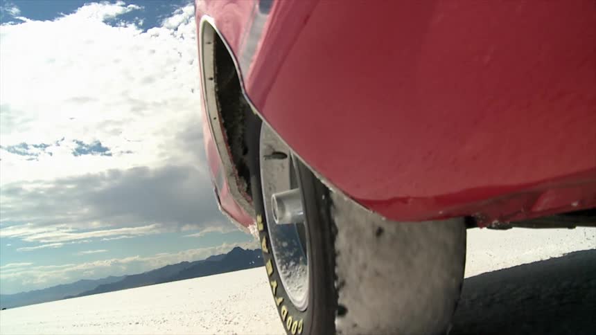 A late model american car is driving on a salt flat in the desert