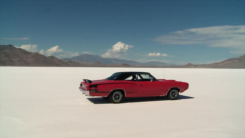 A late model american car is driving on a salt flat in the desert