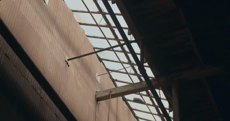 Ropes hang from rafters in a tattered warehouse building