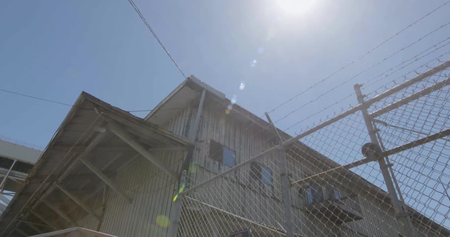 An old building with a chain link fence is filmed from the outside