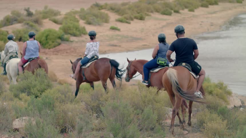 A group of tourists ride horses on a beach during the day