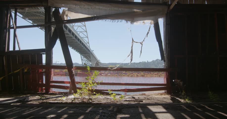 An abandoned shack is filmed while looking out of the opening towards a bridge and river
