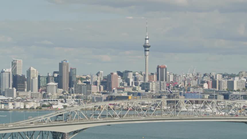 A bridge above a large body of water with a city in the background and clouds in the sky