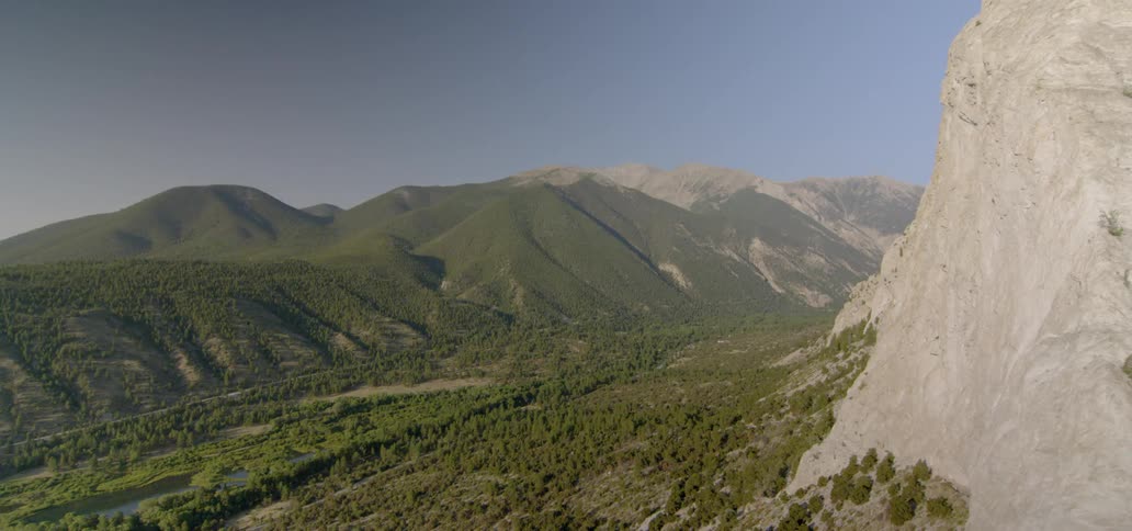 Green trees and plants cover the foot of a stone mountain