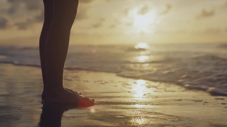Person stands on the beach and water splashes over their feet