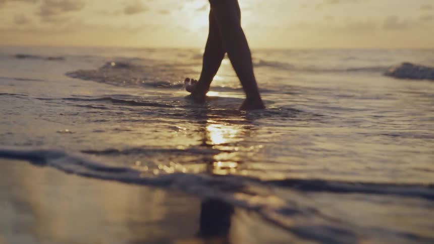Woman walks barefoot over the sand and into the water