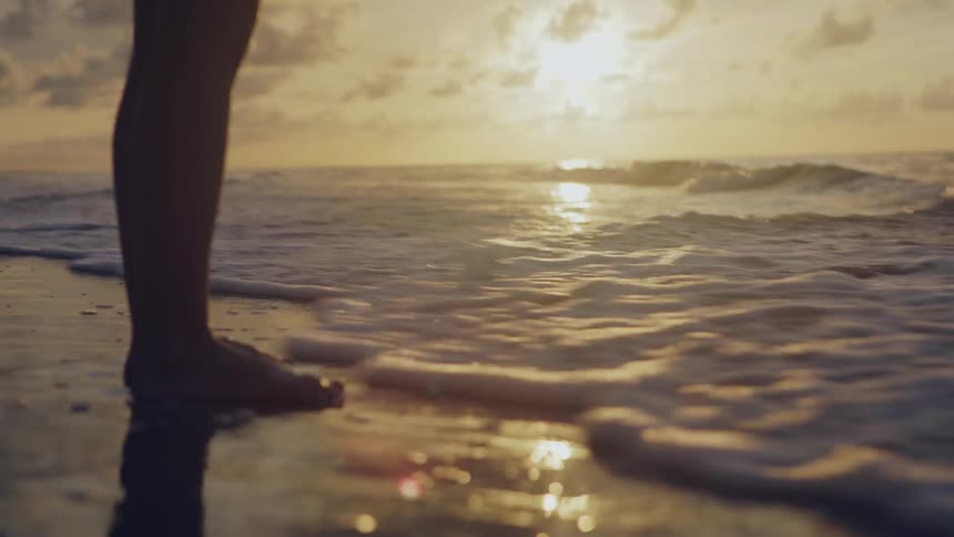 A person stands on the beach as waves wash over their feet