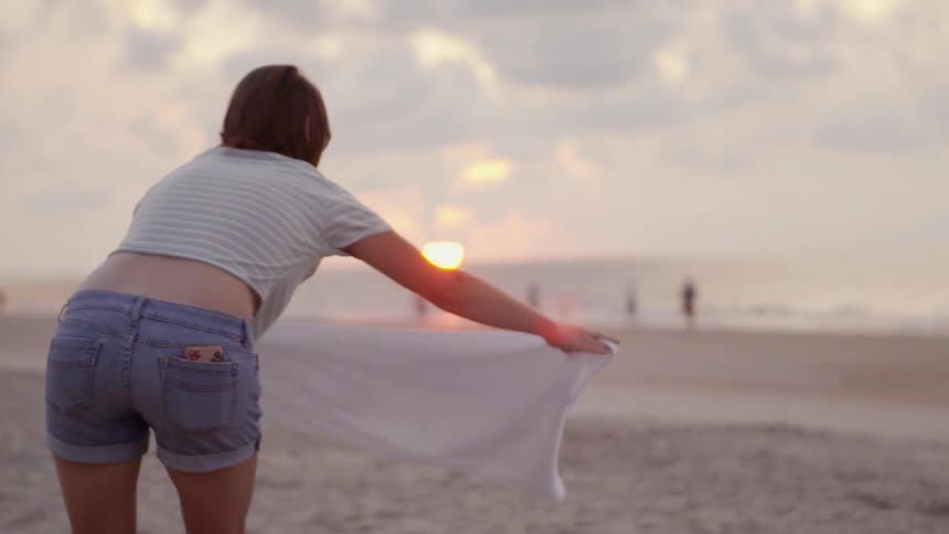 A woman lays out a sheet on the sand