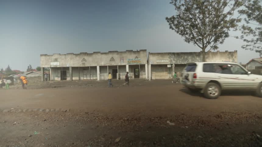 Cars, motor bikes and pedestrians travel on a busy dirt road