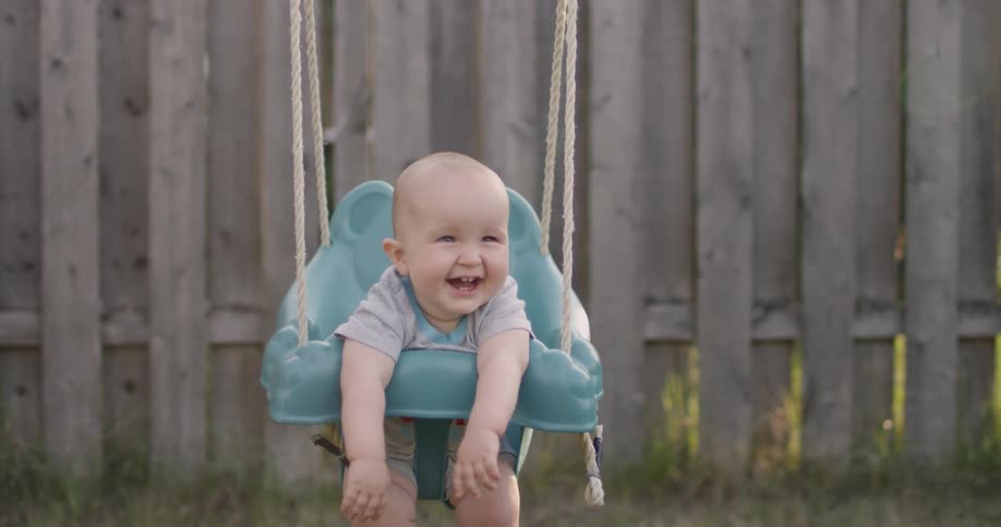 A baby is sitting in a backyard swing grinning large