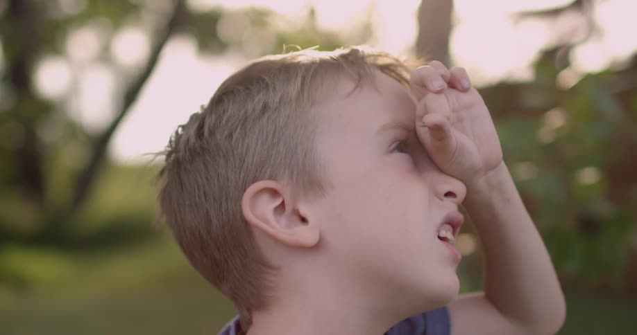 A young boy holds his hand to his eye outside