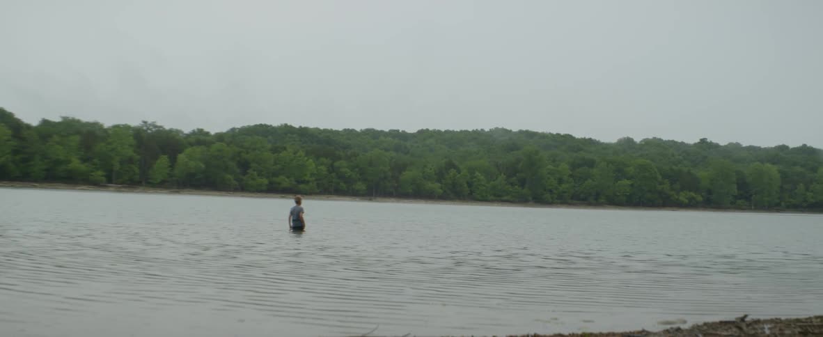 A person is wading in the water on a cloudy day