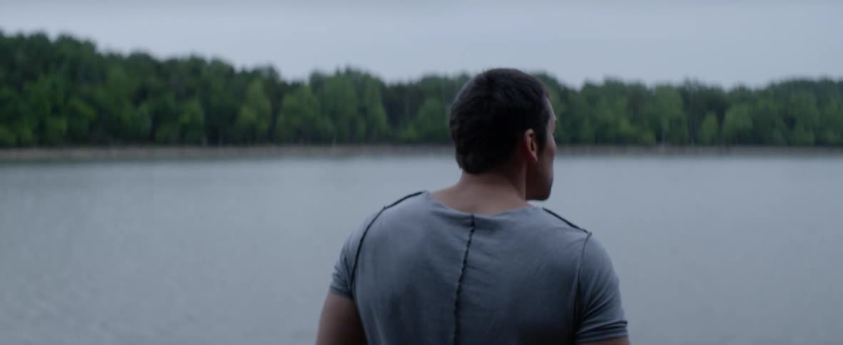 A man stands by the lake on a cloudy day rubbing his head