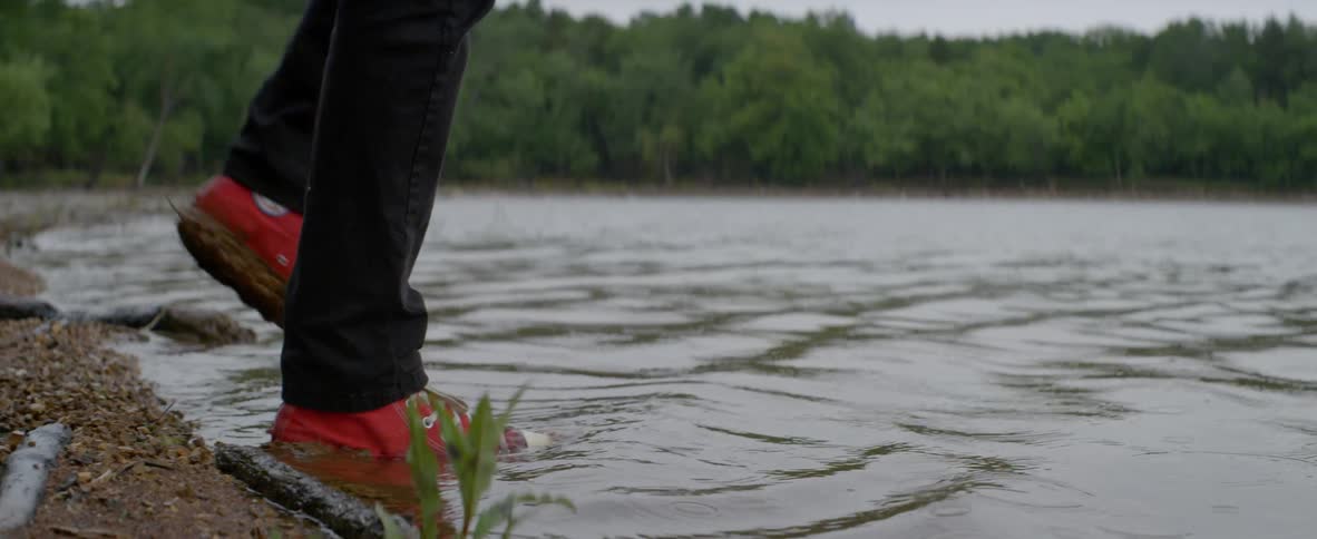 A man wearing red shoes walks into the water