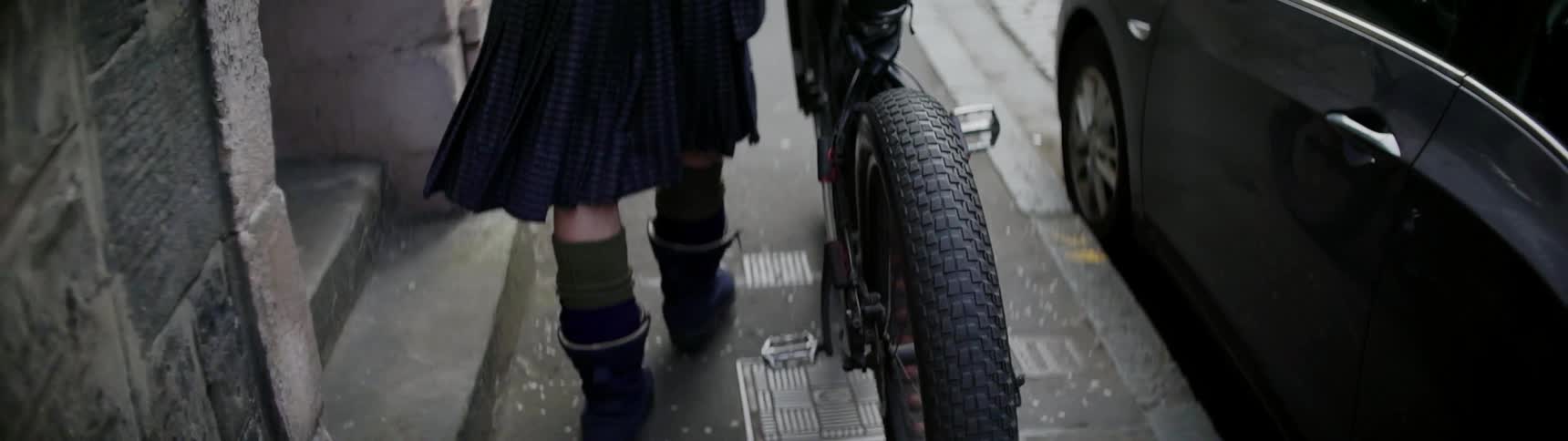 Man walks next to a bike while wearing a kilt