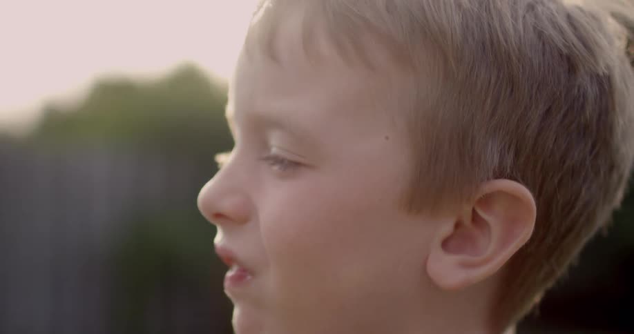 A little blond boy smiles outside in the sun