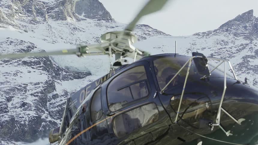 A black helicopter is starting up for take off on the mountain