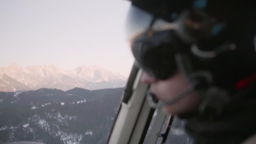 A man is riding in a helicopter over the mountains