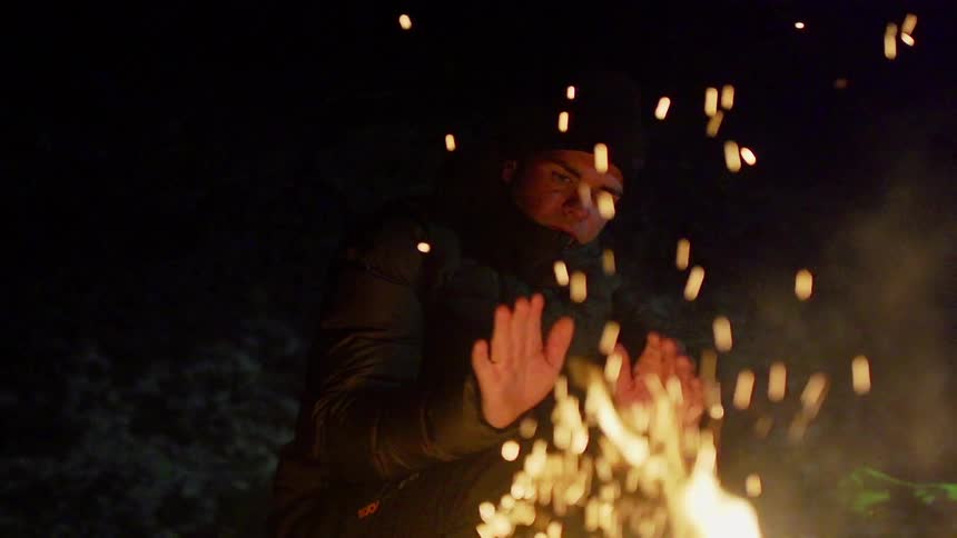 Sparks are flying from a fire as someone is trying to warm their hands