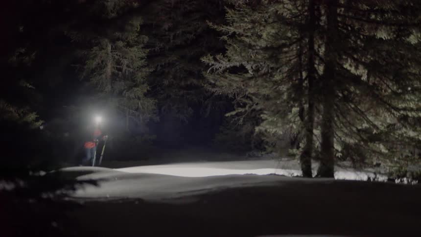 A man walks through the snow with a bright headlamp