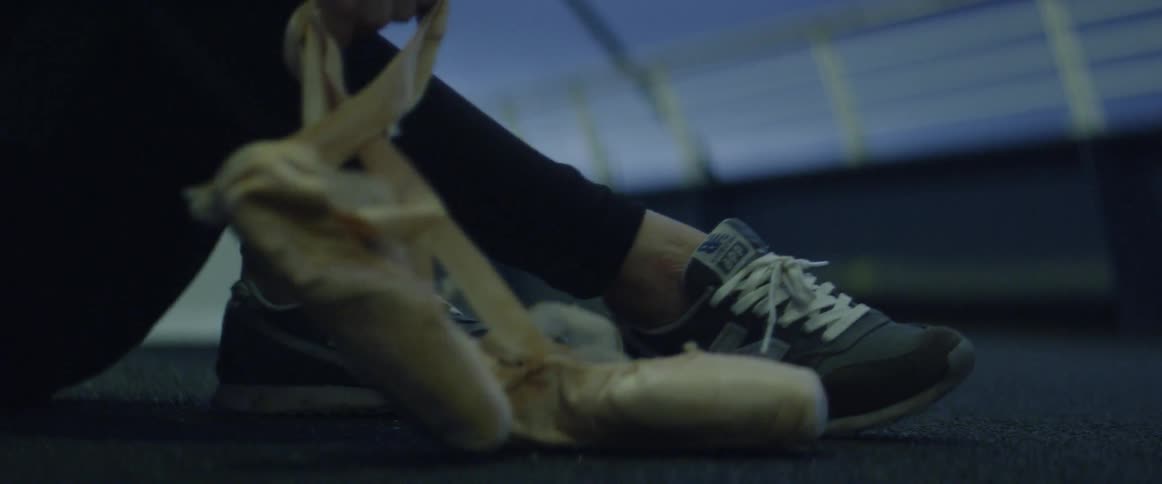 Ballerina sits down to put on pointe shoes
