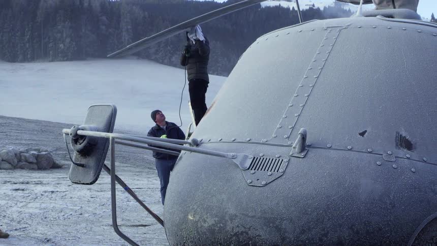 Two men inspect a helicopter parked in the snow