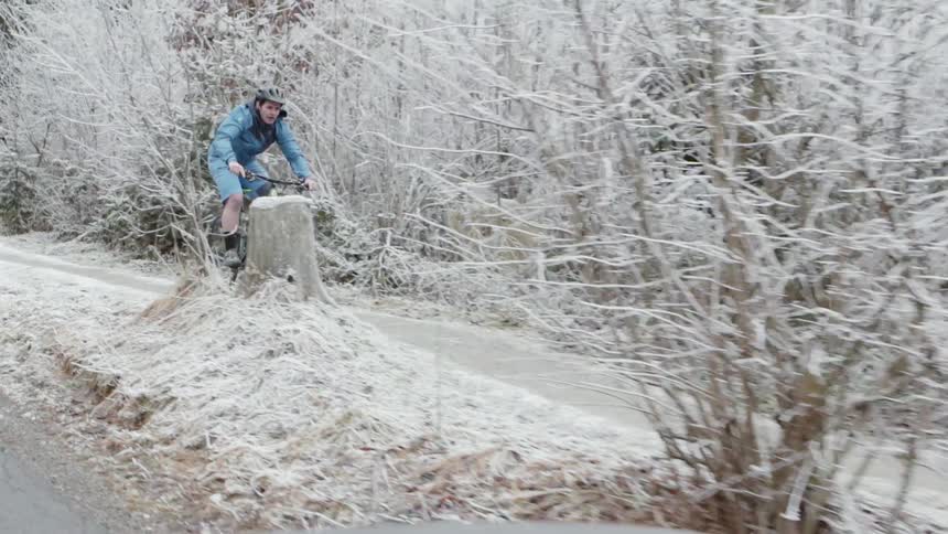 A man is riding a wheelie on his bike through a snow covered trail