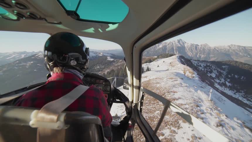 A helicopter is piloted over snowy mountains