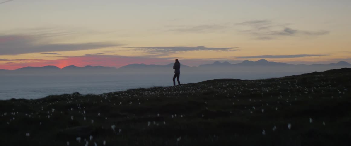 A woman is standing on a cliff side that overlooks a valley