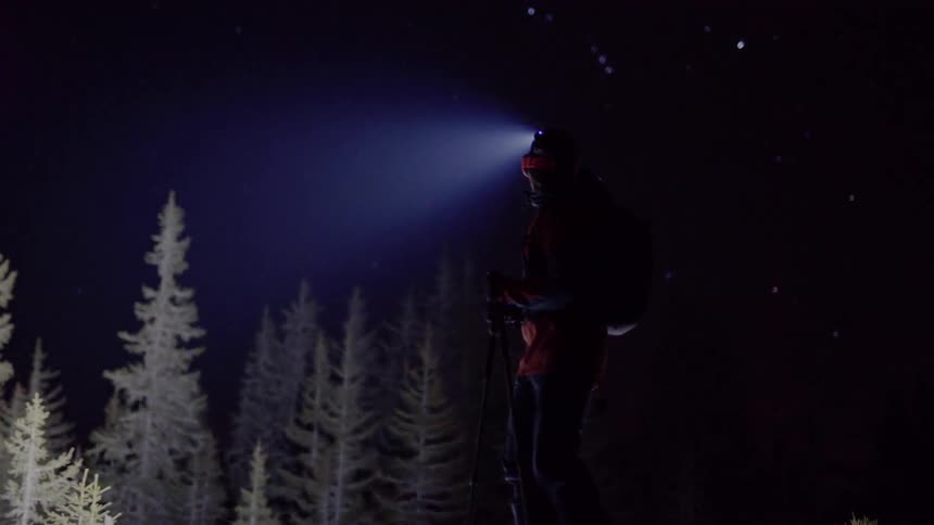 Hiker looks around at frosty trees with headlamp illuminating the night