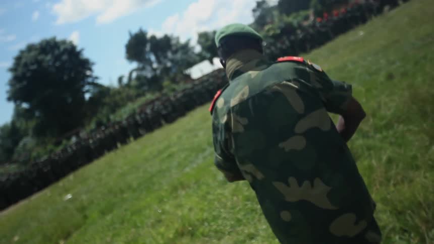 Soldier walks across a grass field towards a large number of troops