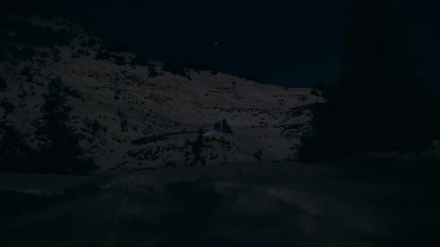 A man hikes with snow shoes and a headlamp