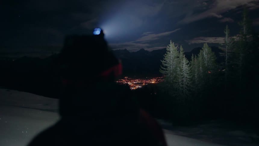A hiker stands in the dark with a headlamp