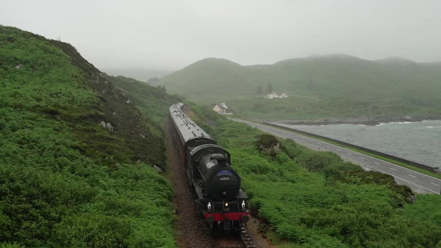 A train travels next to a lake on a misty day