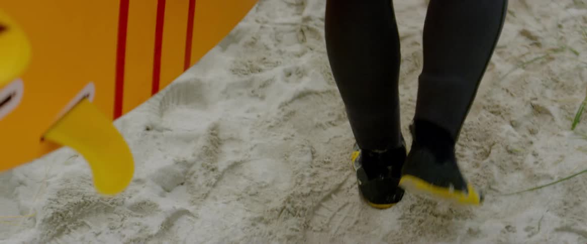 A man in a wetsuit carries a surfboard as he walks over the sand