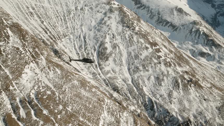 A helicopter flies over snowy mountains