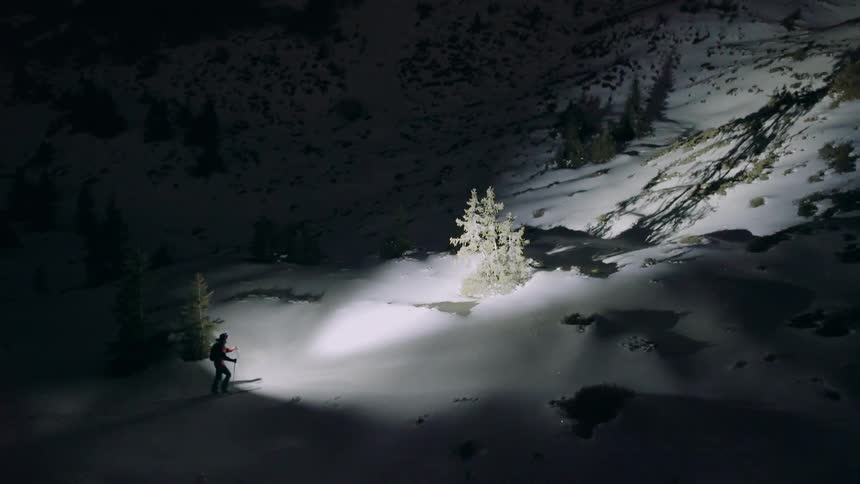 A hiker climbs with snowshoes and a headlamp