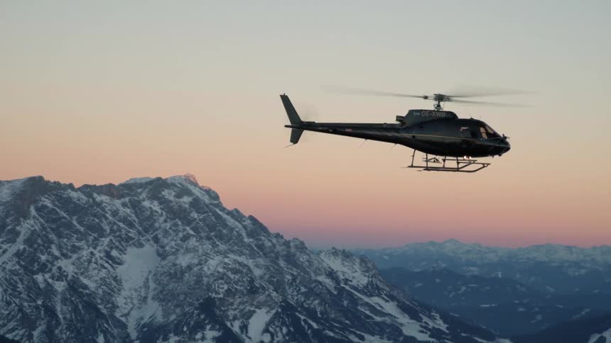 A helicopter is flying above the mountains at dusk