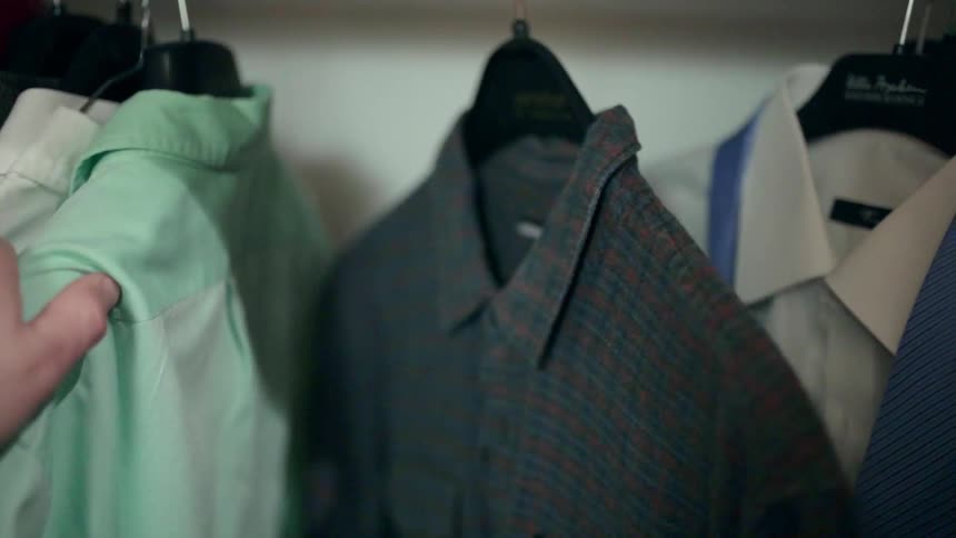 Person moving shirts out of the way on a rack
